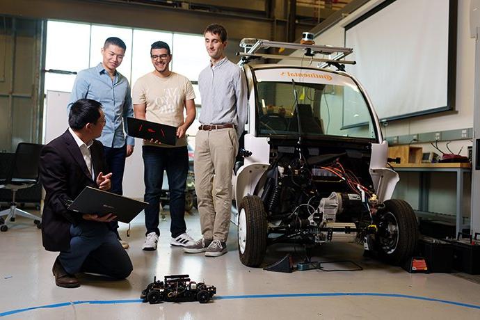 一位教授和三个学生在看一辆机器人汽车
